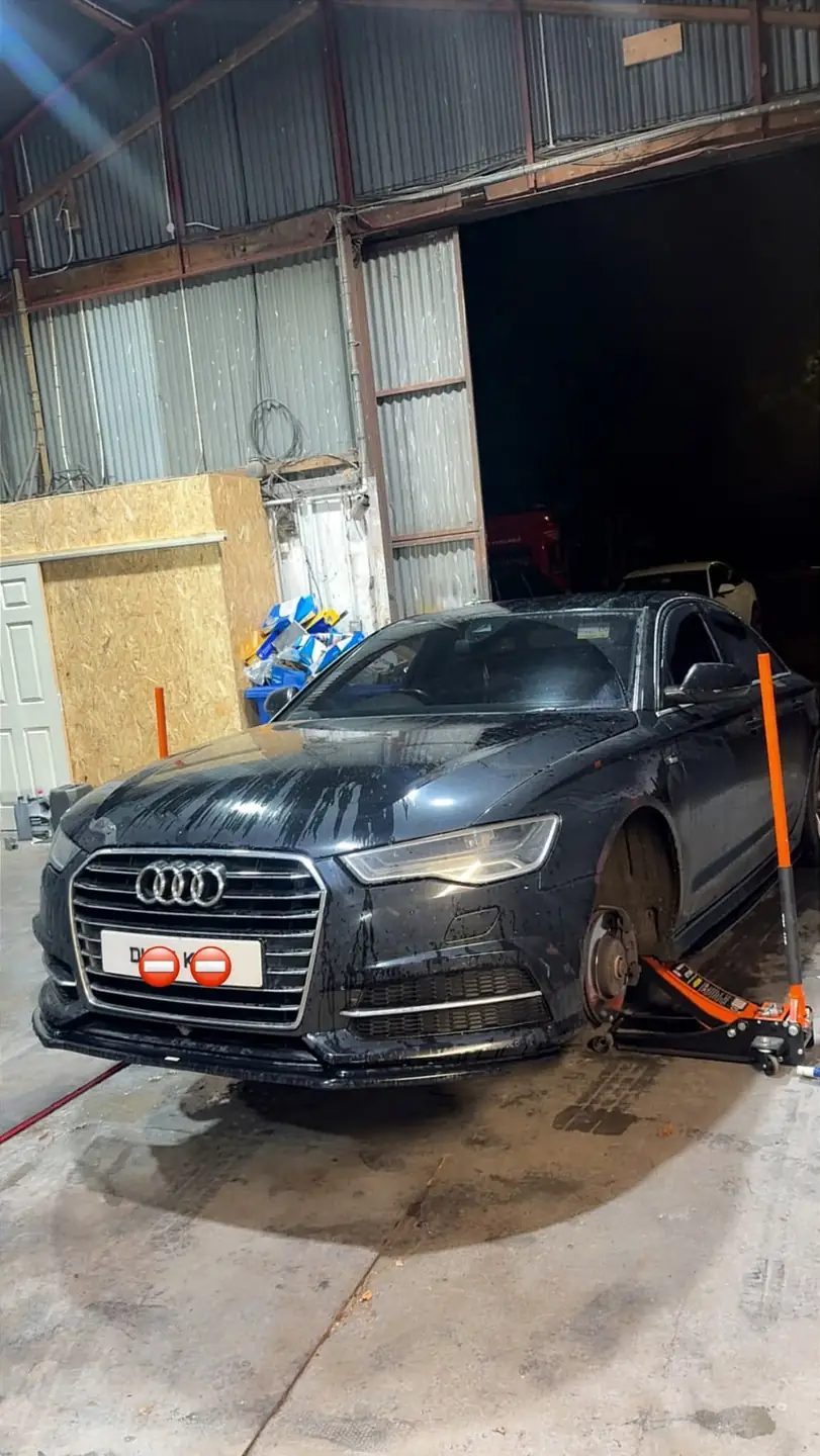 Black Audi A6 on a trolley jack in the Auto Lab workshop with its front wheel off for new brake pads and discs