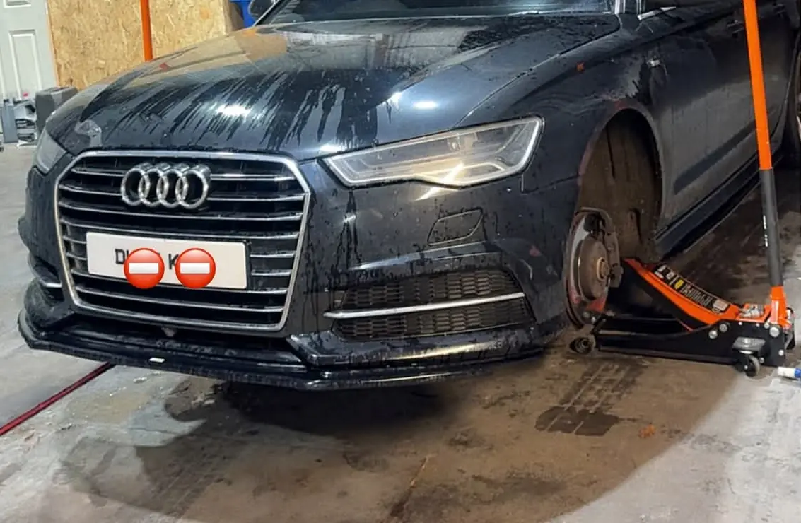 Front end of a black Audi A6 with a black front splitter, in the Auto Lab workshop