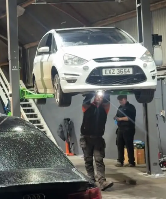 Two Auto Lab technicians working underneath a white Ford S-Max raised on a two-post lift